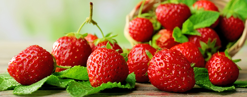 Ripe strawberries with leaves in wicker basket on wooden table on blurred background