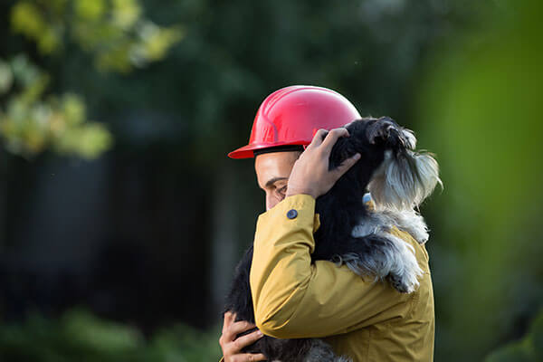 Young man in raincoat and with helmet holding dog in arms. Animal rescue team