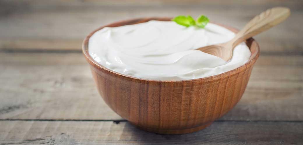 Greek yogurt in a wooden bowl on a rustic wooden table.