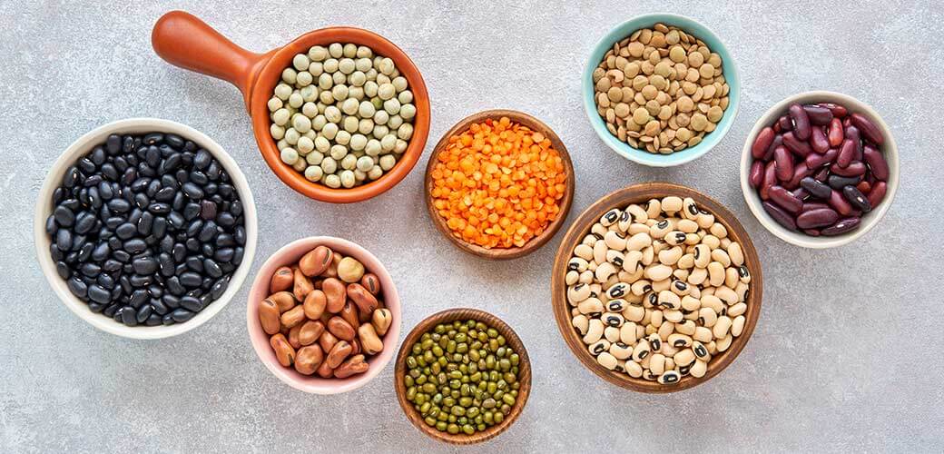 Legumes and beans assortment in different bowls on light stone background