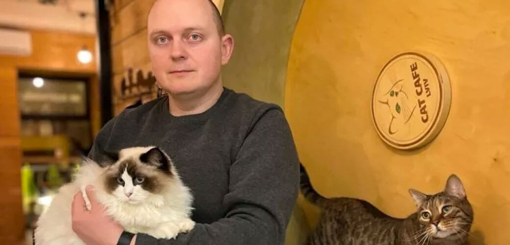 Owner, Serhii Oliinyk holding a white fluffy cat, while a gray tabby cat is standing next to them.