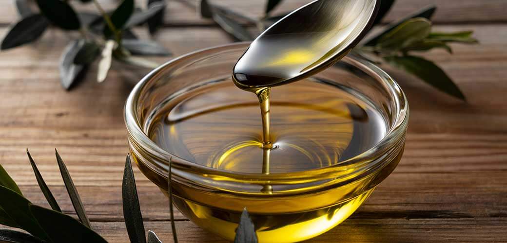 Spooning olive oil into a bowl placed on a wooden background.