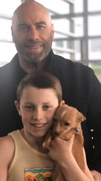 John Travolta and his son with Mac N Cheese. The kid is holding the puppy, while Travolta is behind them.