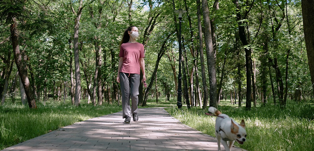 Young woman in protective mask on his face walking in Park with small dog Chihuahua.